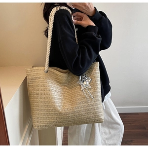 Detail of handwoven straw tote bag featuring rope handles and a silver star charm