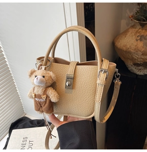 Detail of cream white bucket bag in lychee pattern leather with a cute plush bear charm