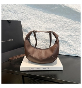 Detail of a brown leather crescent shoulder bag with lychee texture on art books