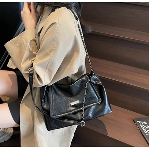 Detail of black glossy crinkled leather texture and silver chain strap on crossbody bag