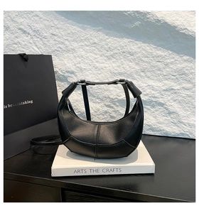 Detail of black crescent leather bag with lychee texture and silver hardware on white book