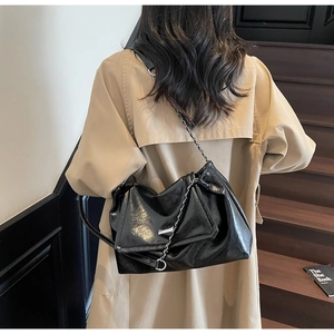 Detail of a large black glossy tote bag with stylish pleated design and silver chain straps