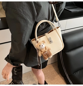 Detail of creamy white bucket bag in lychee leather with cute bear doll accessory