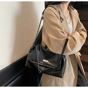 Detail shot of black glossy shoulder bag with silver chain strap on a trench coat