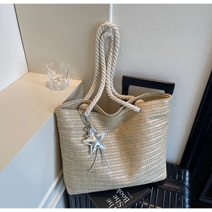 Close-up of woven straw tote bag with white rope handles and silver star charm detail