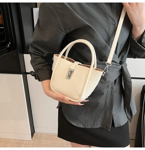 Close-up of off-white lychee grain leather bucket bag with silver square buckle and strap