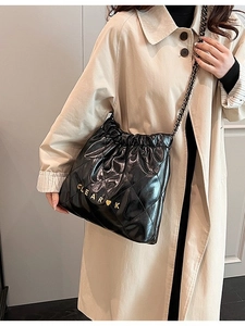 Chic black quilted bucket bag with gold chain strap and heart logo on beige coat