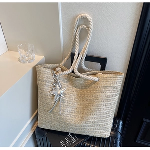 Detail of beige woven straw tote bag with cotton rope handles and silver star pendant