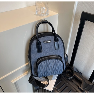 Detail of denim and leather backpack featuring quilted front pocket and metal brand logo
