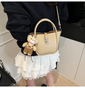 Detail of cream beige leather bucket bag with metal turn-lock and plush bear charm