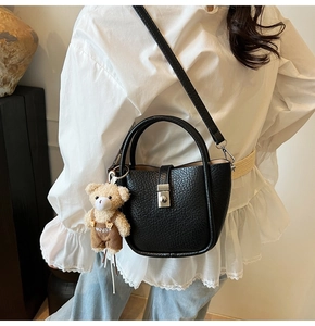 Detail of black lychee grain leather bucket bag with cute plush bear charm and metal lock