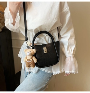 Detail of black textured leather bucket bag with silver twist lock and a cute bear charm