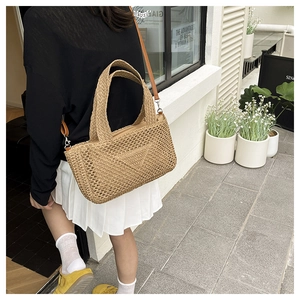 Close-up of a hollow-out knit straw tote bag with leather strap in an outdoor setting