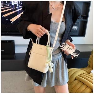 Detail of cream mini bucket bag with tulip charm and fine shoulder strap on a model