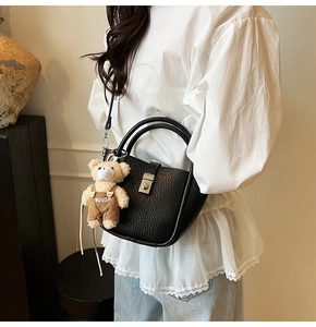 Detail of black lychee grain leather bucket bag with round handle and cute bear charm