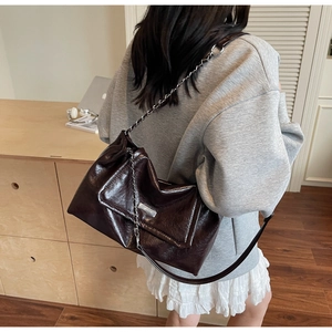 Detail of glossy dark brown leather shoulder bag with silver chain and metal plaque