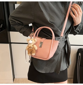 Detailed shot of pink litchi grain bucket bag with teddy bear charm and crossbody strap
