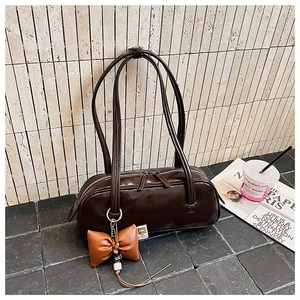 Détail d'un sac baguette cylindrique marron foncé brillant avec nœud en cuir