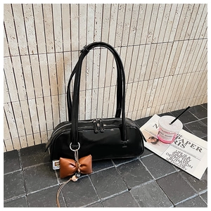 Détail du sac baguette en cuir verni noir avec de fines brides et un nœud décoratif