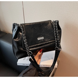 Detail of black glossy pleated shoulder bag with silver chain and metal plate