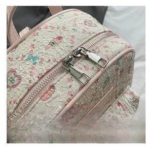 Detail shot of the cream backpack showing floral fabric texture and silver zippers