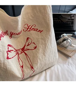Minimalist cream canvas tote bag with red bow print and notebook in lifestyle setting