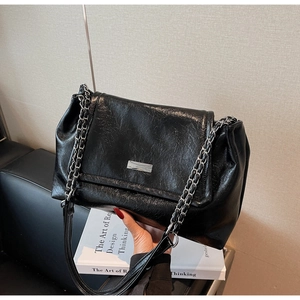 Close-up of black glossy leather shoulder bag with silver chain strap and metal detail