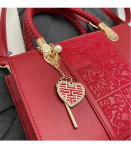 Detail of red bridal handbag featuring floral embroidery and a heart-shaped Xi charm