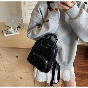 Mirror selfie showing the scale of a black pleated leather mini backpack with a top handle