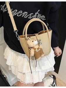 Chic beige lychee textured bucket bag with bear pendant and silver twist lock detail