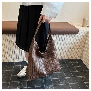 Detailed view of dark brown hand-woven Intrecciato leather tote bag held by model