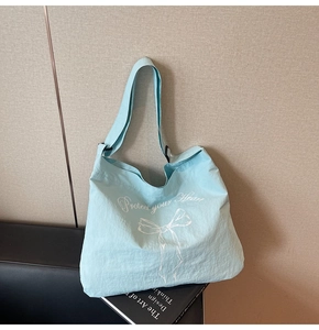 Detail of light blue canvas tote bag featuring white bow print and stylish shoulder strap
