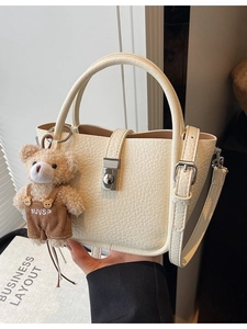 Minimalist beige pebble leather bucket bag with teddy bear charm and metal buckle