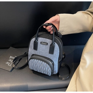 Detail of grey fabric backpack with pleated black front pocket and leather handle