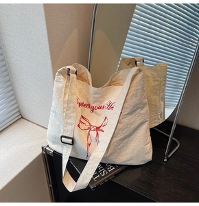 Detail view of cream canvas tote bag with red ribbon print and adjustable black strap