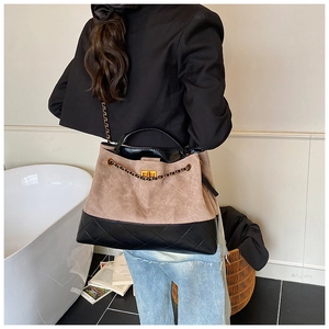 Détail d'un sac cabas en daim kaki et cuir matelassé noir avec un fermoir rotatif doré