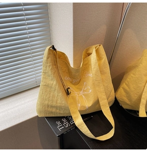 Detail of a yellow canvas tote bag featuring a white bow print and adjustable black buckle strap