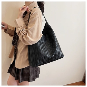 Detail of a large black woven leather tote bag showing intricate texture and crossbody fit
