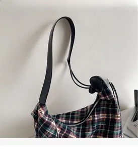 Détail montrant la texture du tissu écossais rétro et la bandoulière en cuir du sac cabas