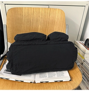Detail of black nylon messenger bag with puff pleated fabric and front flap pockets on a chair