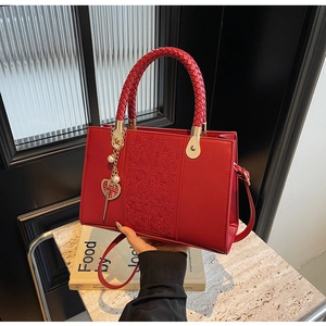 Detail of red leather handbag with floral embossing, woven handle, and heart pendant