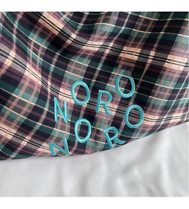 Gros plan du logo NORO brodé sur le sac seau en tissu à carreaux pour femmes