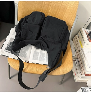 Detail of a black nylon crossbody bag with multiple pockets on a wooden chair