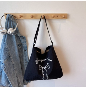 Detail of black canvas tote bag with white bow print and Greet your heart cursive text