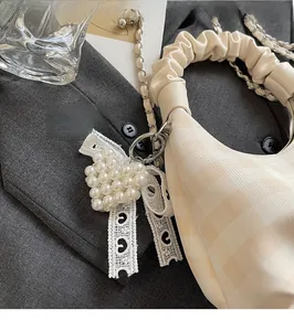 Detail of heart-shaped pearl pendant and lace ribbon on checkered crossbody bag
