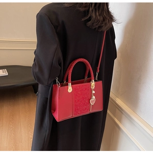 Detail of red bridal handbag with woven handle and golden heart charm on black coat