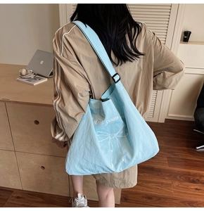 Close-up of light blue shoulder bag featuring a white bow print and adjustable strap buckle