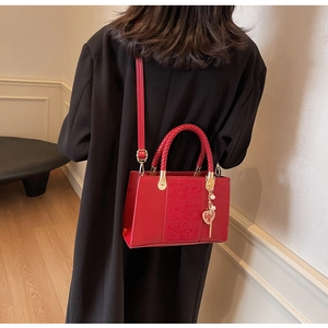Detailed embroidery on red bridal handbag with woven handle and gold heart charm