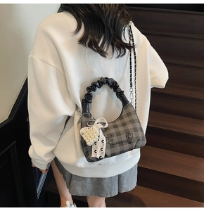 Detail of grey plaid handbag with ruffled handle and pearl heart charm on stairs