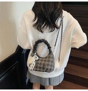 Detail of checkered crossbody bag with pearl bow charm and black chain strap shown on model